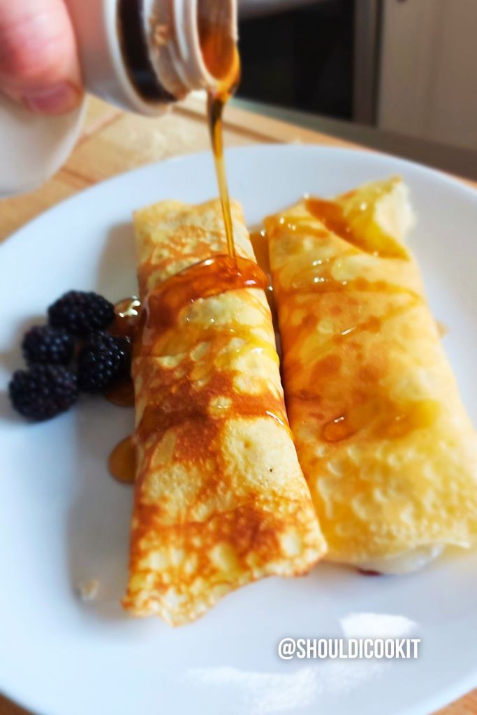 Pouring maple syrup over cooked crepes on the plate